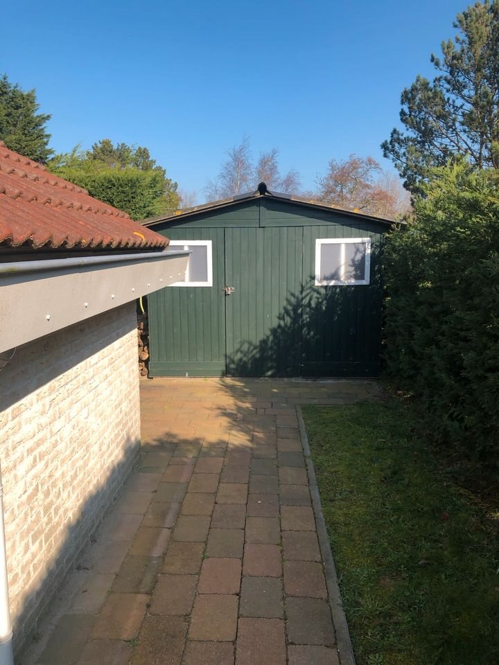 Gepflasterte Zufahrt mit grünem Holzschuppen